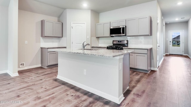 kitchen featuring gray cabinets, a kitchen island with sink, black gas stove, and sink