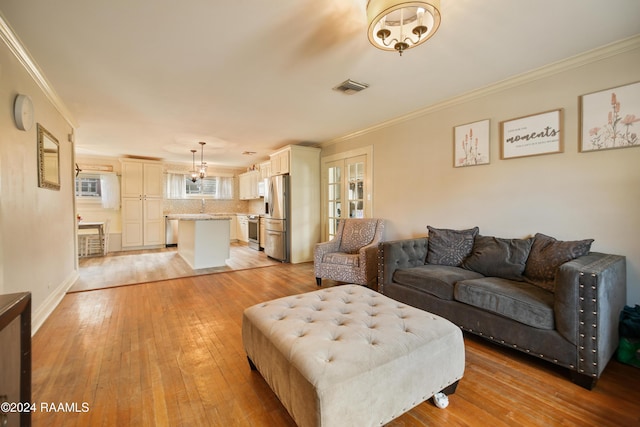 living room with a chandelier, ornamental molding, and light hardwood / wood-style flooring