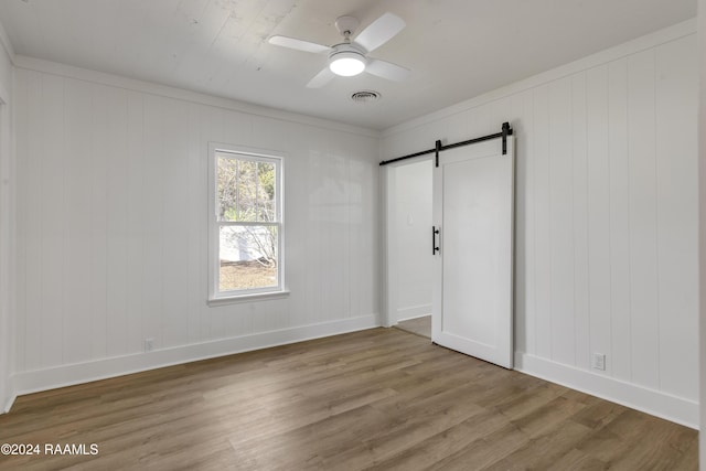 unfurnished bedroom with hardwood / wood-style floors, ornamental molding, a barn door, and ceiling fan