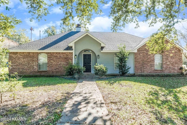 single story home featuring brick siding, a front lawn, a shingled roof, and a chimney