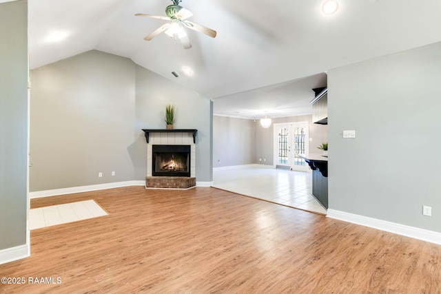 unfurnished living room with baseboards, a tile fireplace, vaulted ceiling, and light wood-type flooring