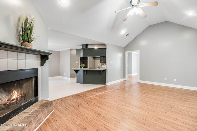 unfurnished living room with baseboards, vaulted ceiling, wood finished floors, a ceiling fan, and a lit fireplace