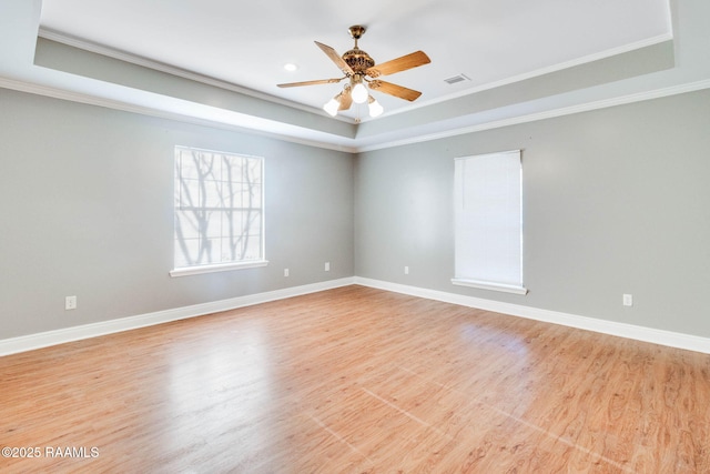 empty room featuring light wood-style flooring, baseboards, visible vents, and a tray ceiling