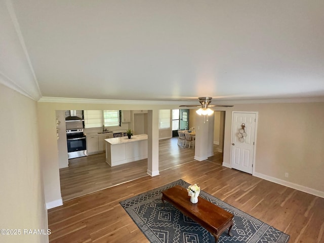 living area featuring baseboards, ornamental molding, wood finished floors, and a ceiling fan
