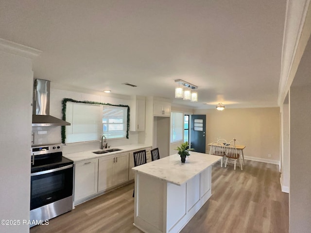 kitchen featuring a sink, stainless steel electric range, light wood-style flooring, wall chimney range hood, and white cabinets