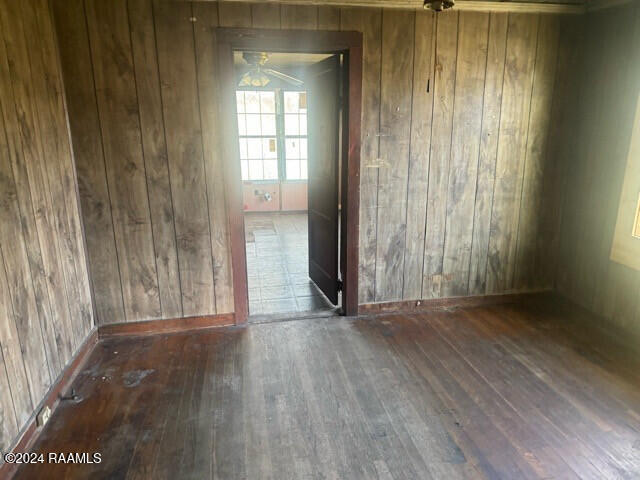 unfurnished room featuring ceiling fan, wood walls, and dark wood-type flooring