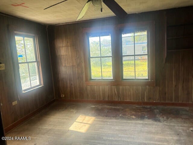 empty room with ceiling fan, wood-type flooring, and wooden walls