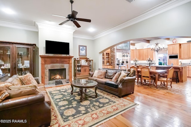 living room featuring light hardwood / wood-style flooring, a high end fireplace, ceiling fan with notable chandelier, and ornamental molding