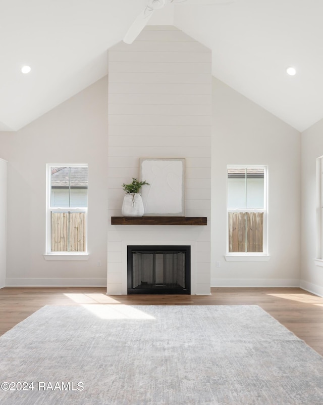 unfurnished living room featuring a large fireplace, high vaulted ceiling, and light wood-type flooring