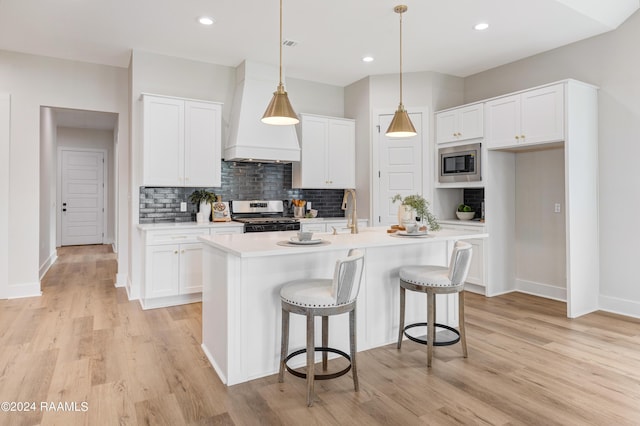 kitchen featuring white cabinets, decorative light fixtures, a kitchen island with sink, and appliances with stainless steel finishes