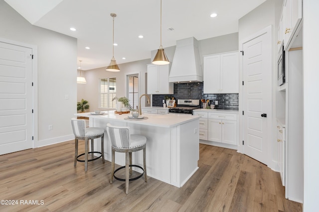 kitchen with a center island with sink, white cabinets, hanging light fixtures, appliances with stainless steel finishes, and custom range hood