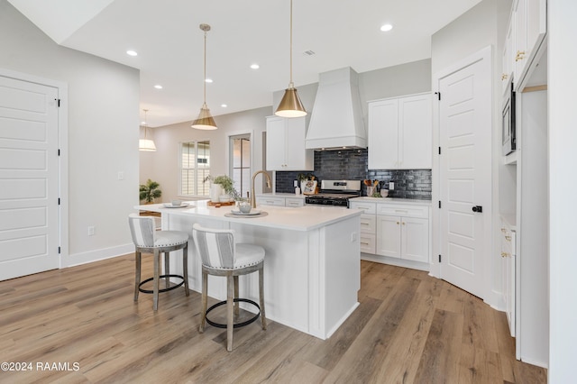 320 Dunvegan Ct, Lafayette, LA 70503 - kitchen with custom range hood, stove, light wood-style flooring, backsplash, and a kitchen bar