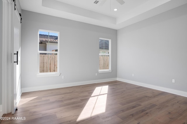 spare room featuring a tray ceiling, a barn door, ceiling fan, and light hardwood / wood-style floors