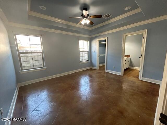 unfurnished bedroom with a walk in closet, multiple windows, and a tray ceiling