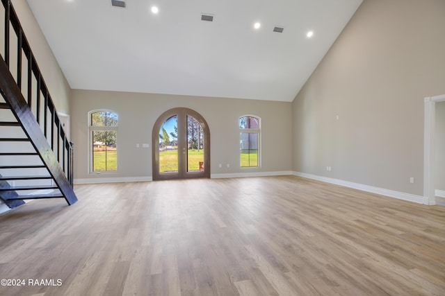 unfurnished living room with french doors, high vaulted ceiling, and light wood-type flooring