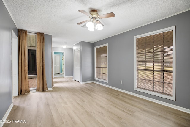 empty room with a textured ceiling, ceiling fan, a wealth of natural light, and light hardwood / wood-style flooring