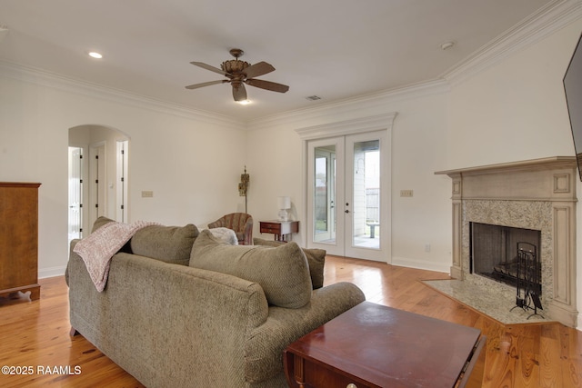 living room featuring ceiling fan, french doors, a premium fireplace, light hardwood / wood-style floors, and ornamental molding