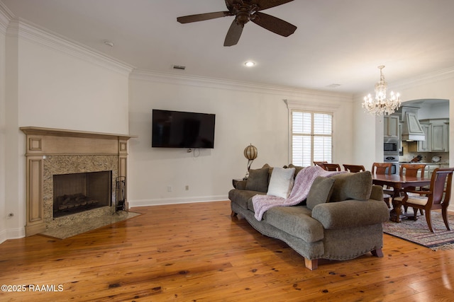 living room featuring ornamental molding, ceiling fan with notable chandelier, a high end fireplace, light wood-style floors, and baseboards