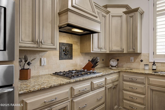 kitchen featuring light stone counters, premium range hood, backsplash, and stainless steel gas cooktop