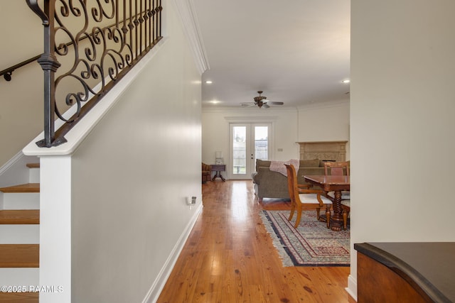 hall featuring light wood finished floors, baseboards, stairs, ornamental molding, and french doors