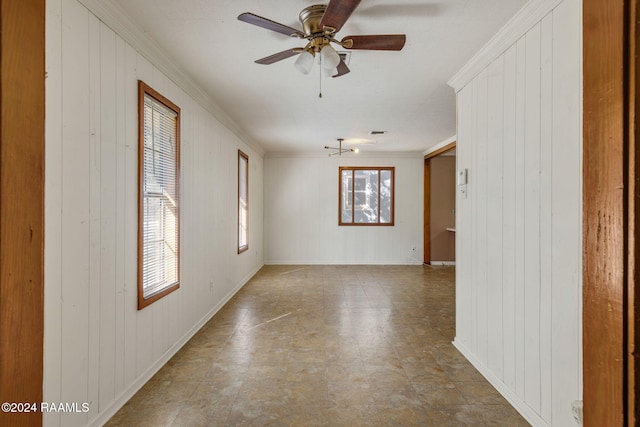 empty room featuring crown molding, ceiling fan, a healthy amount of sunlight, and wood walls