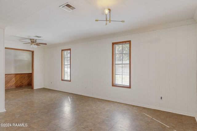 spare room with crown molding, wooden walls, and ceiling fan with notable chandelier