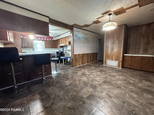 kitchen with a kitchen bar, pendant lighting, kitchen peninsula, and wood walls