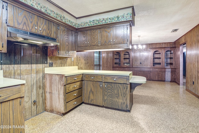 kitchen featuring kitchen peninsula, wood walls, ornamental molding, and a notable chandelier