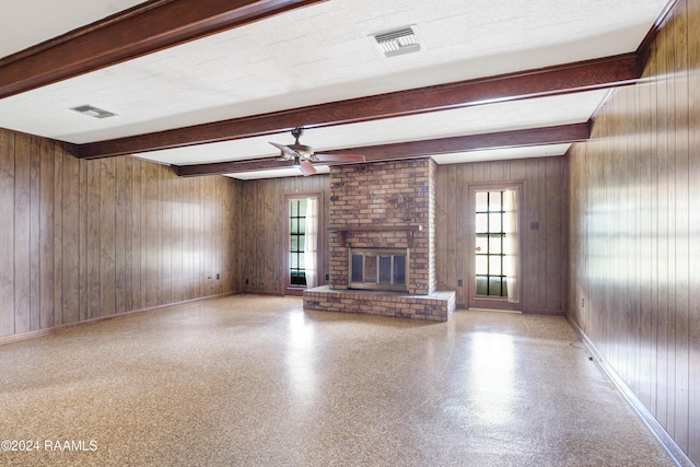 unfurnished living room with beam ceiling, wooden walls, a fireplace, and ceiling fan