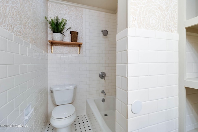 bathroom featuring tile patterned flooring, tiled shower / bath combo, toilet, ornamental molding, and tile walls