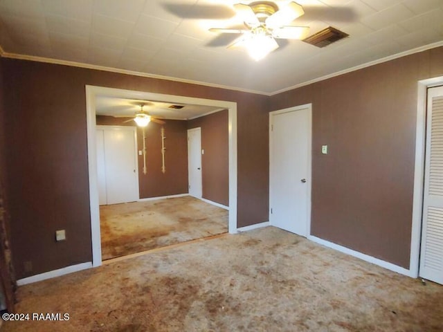 carpeted spare room featuring baseboards, visible vents, a ceiling fan, and crown molding