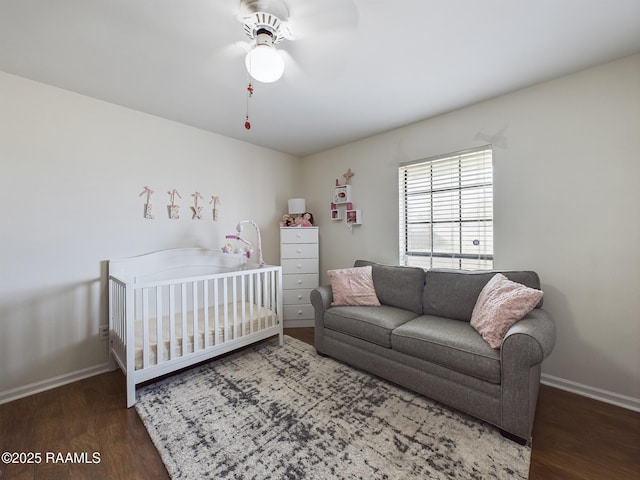 bedroom with ceiling fan, a nursery area, and dark hardwood / wood-style flooring