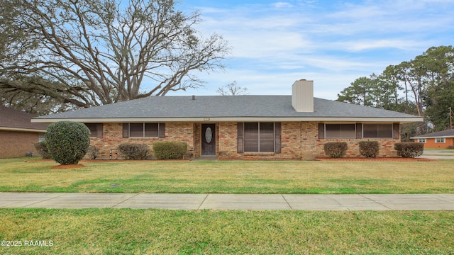 ranch-style house featuring a shingled roof, a chimney, a front lawn, and brick siding