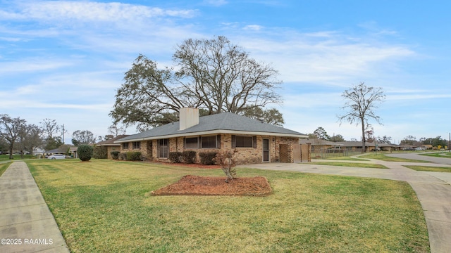 view of front of house featuring brick siding, driveway, a chimney, and a front lawn