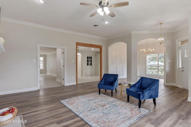 living area with ceiling fan with notable chandelier, wood-type flooring, and ornamental molding