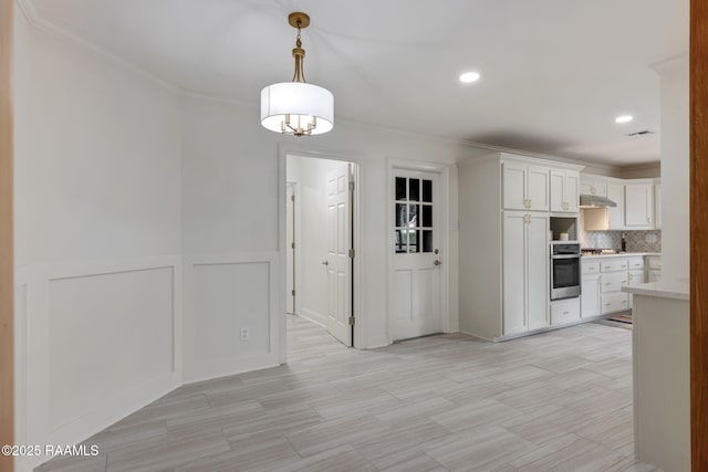 kitchen featuring tasteful backsplash, ornamental molding, decorative light fixtures, oven, and white cabinetry