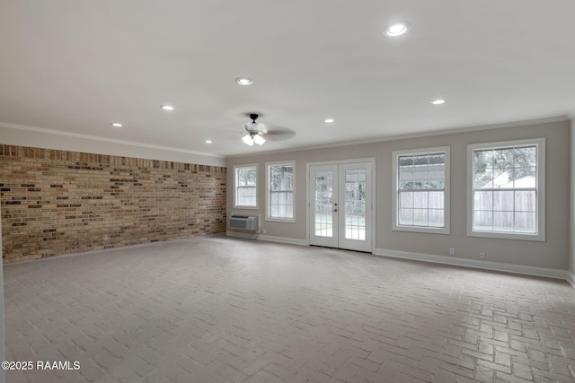 unfurnished living room with french doors, crown molding, ceiling fan, brick wall, and a wall unit AC