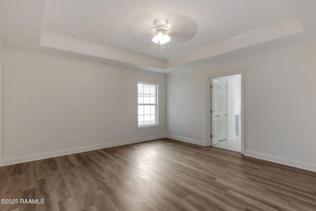 empty room with dark wood-type flooring, a tray ceiling, and ornamental molding