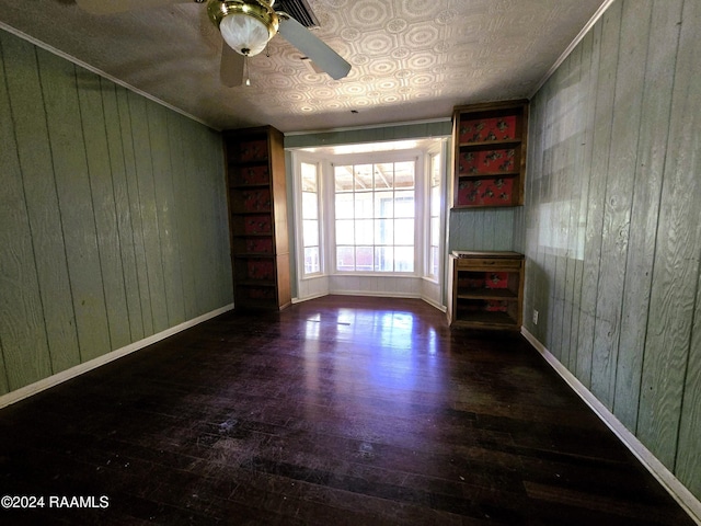 empty room with ceiling fan, dark wood-type flooring, crown molding, a textured ceiling, and wooden walls