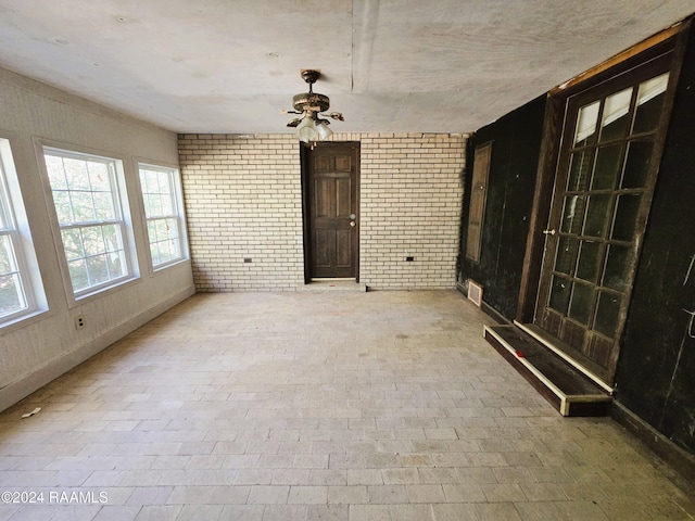 empty room featuring ceiling fan and brick wall