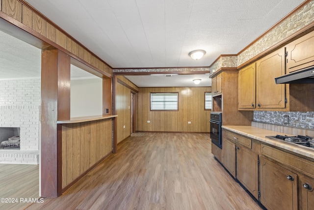 kitchen featuring wood walls, oven, crown molding, light wood-type flooring, and stainless steel gas cooktop