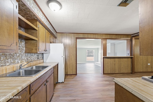 kitchen with sink, wood walls, white fridge, light hardwood / wood-style floors, and decorative backsplash