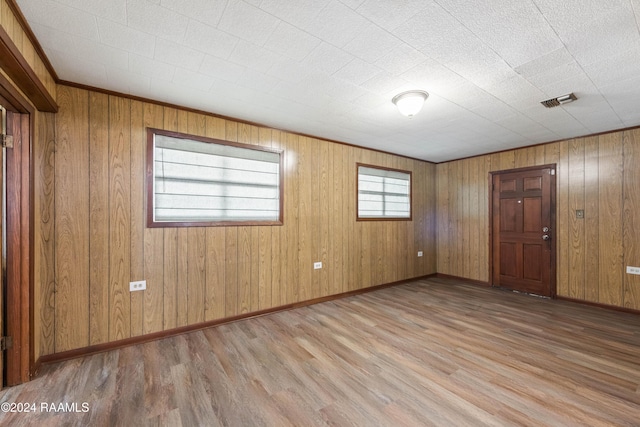 empty room featuring light hardwood / wood-style flooring, ornamental molding, and wood walls