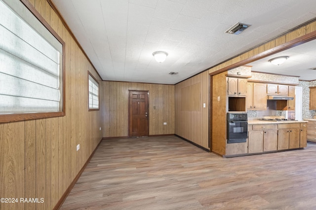 kitchen with wooden walls, oven, light hardwood / wood-style floors, and stainless steel gas stovetop