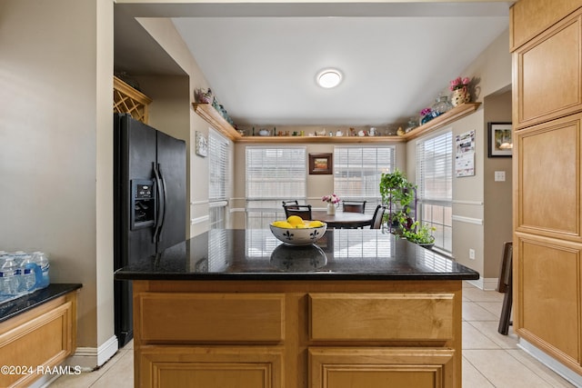 kitchen featuring dark stone counters, black refrigerator with ice dispenser, a kitchen island, and light tile patterned flooring