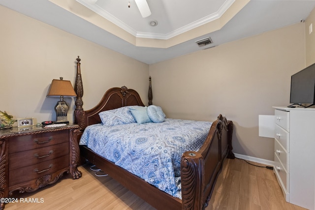 bedroom with a tray ceiling, ceiling fan, crown molding, and light wood-type flooring