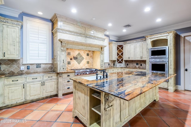 kitchen featuring a kitchen island with sink, dark stone counters, sink, decorative backsplash, and appliances with stainless steel finishes