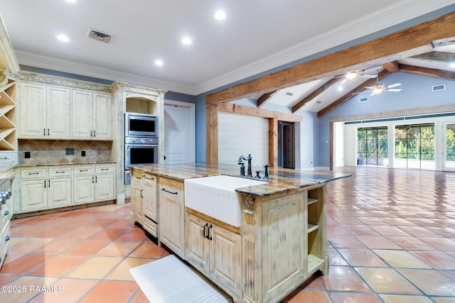 kitchen with decorative backsplash, light stone countertops, a kitchen island with sink, sink, and cream cabinets