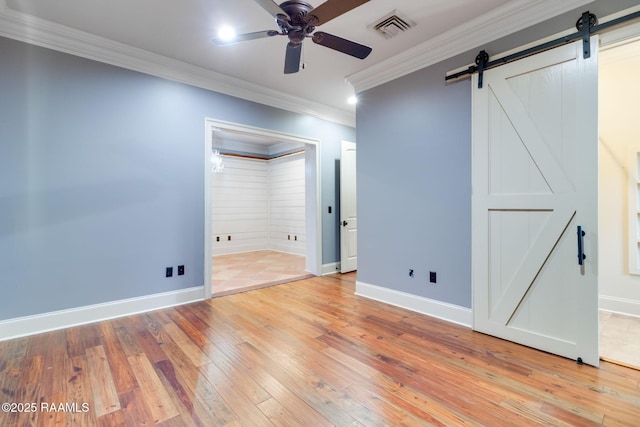 spare room featuring a barn door, ceiling fan, light hardwood / wood-style flooring, and ornamental molding