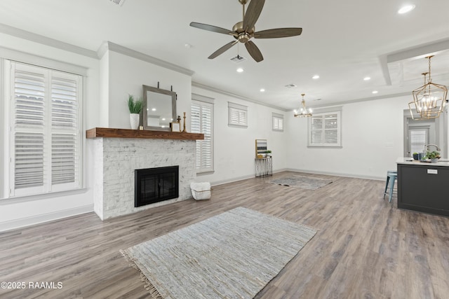 living room with hardwood / wood-style flooring, ceiling fan with notable chandelier, a stone fireplace, and crown molding